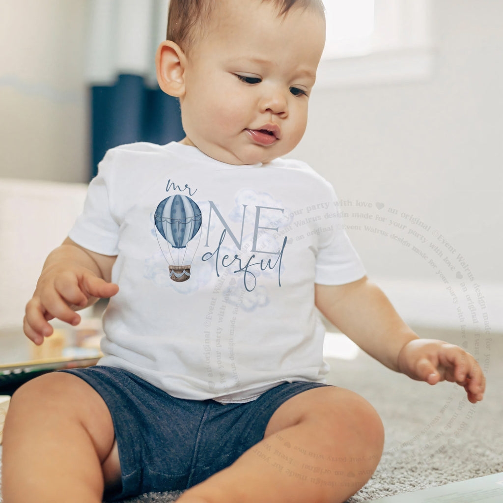 Little boy sitting on a rug in a white Mr Onederful baby tee.
