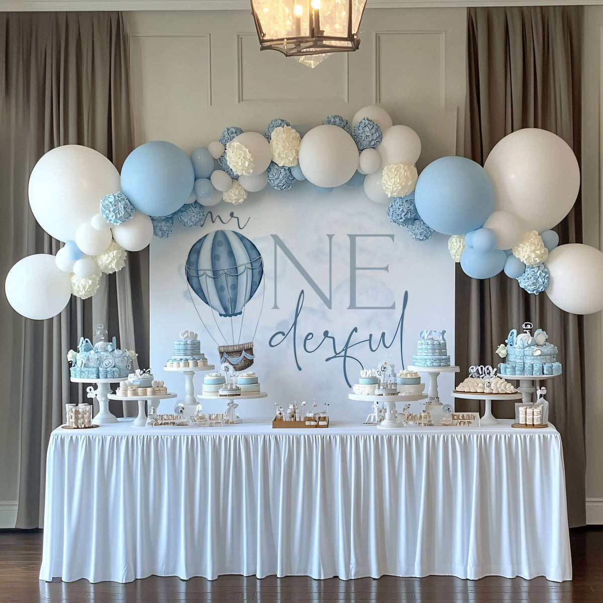 Blue hot air balloon Mr Onederful backdrop behind a dessert table with a white and blue balloon arch.