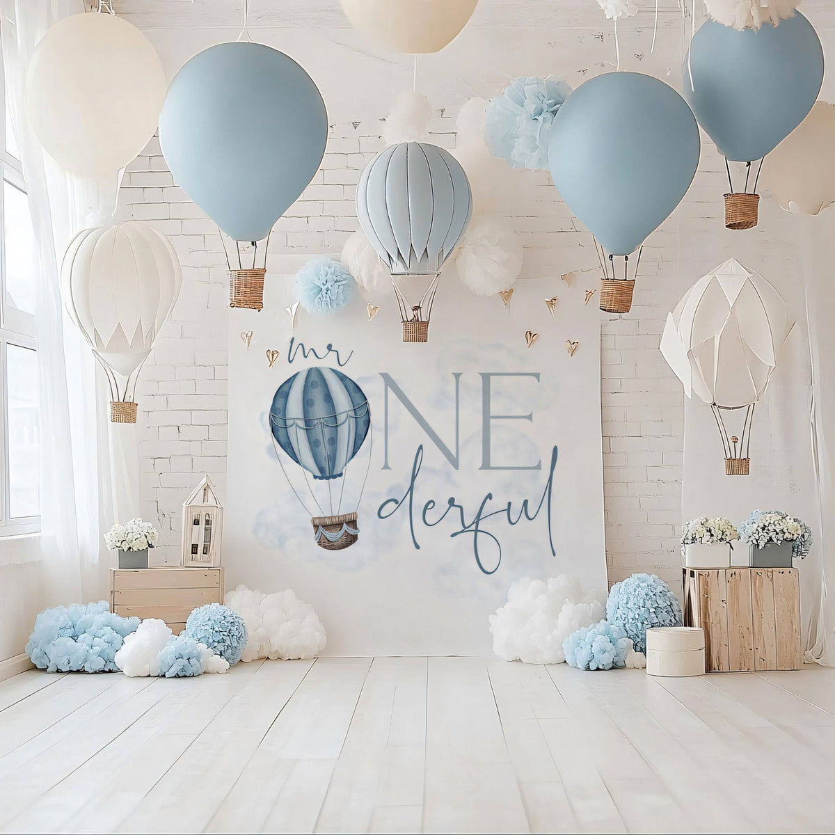 Mr Onederful backdrop on a white wall with hanging paper hot air balloons and blue pom poms.