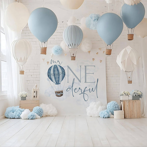 Mr Onederful backdrop on a white wall with hanging paper hot air balloons and blue pom poms.