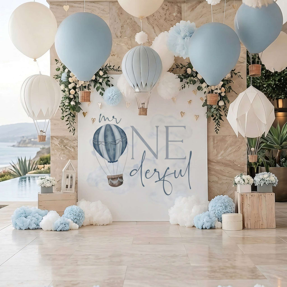 Mr Onederful backdrop at an outdoor first birthday with hanging hot air balloons and blue pom poms.