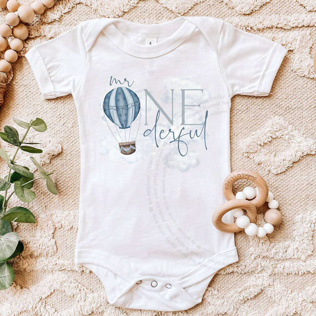 White Mr Onederful first birthday bodysuit on a beige blanket with a wooden teether.