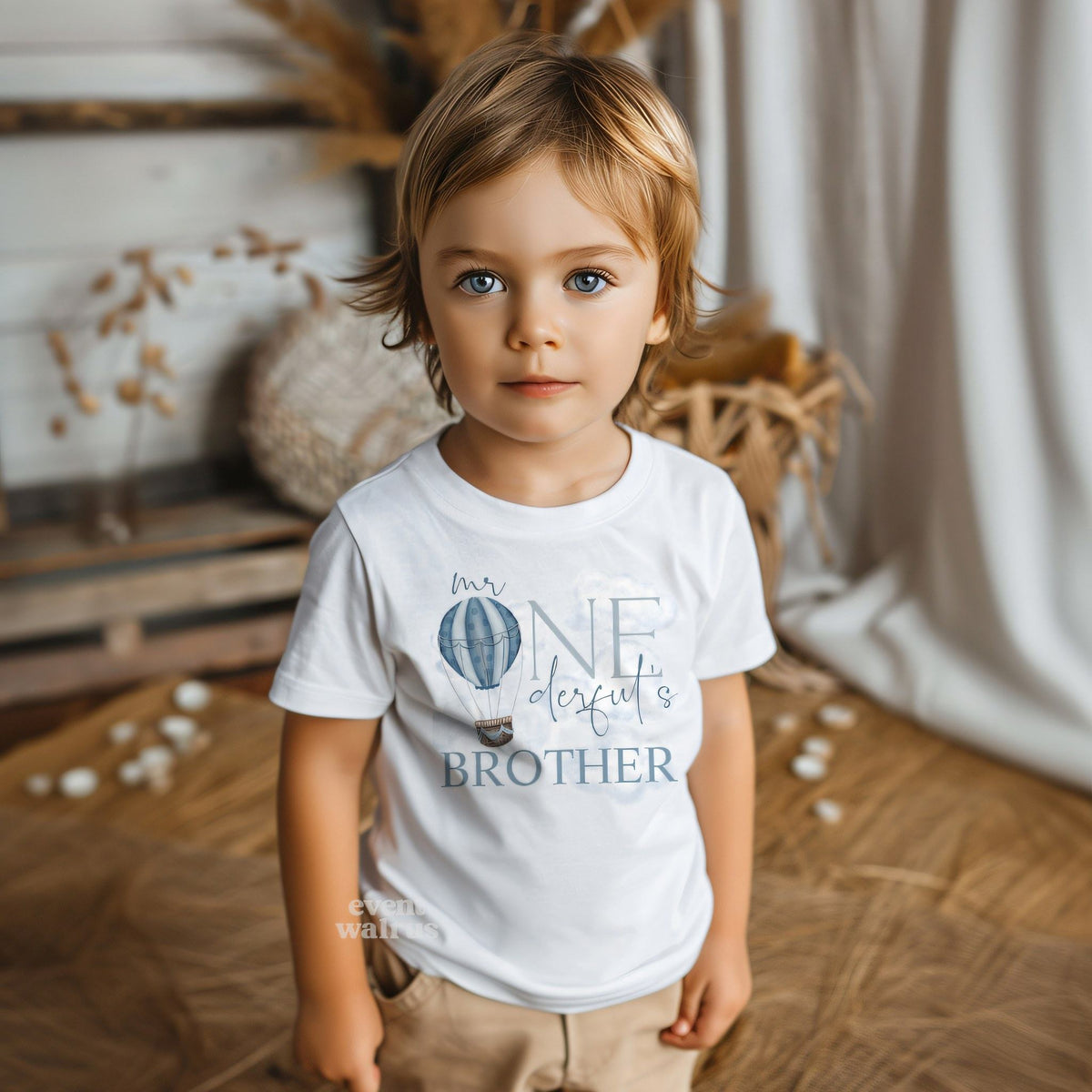 Little boy in a white Mr Onederful's Brother toddler tee in a boho room.