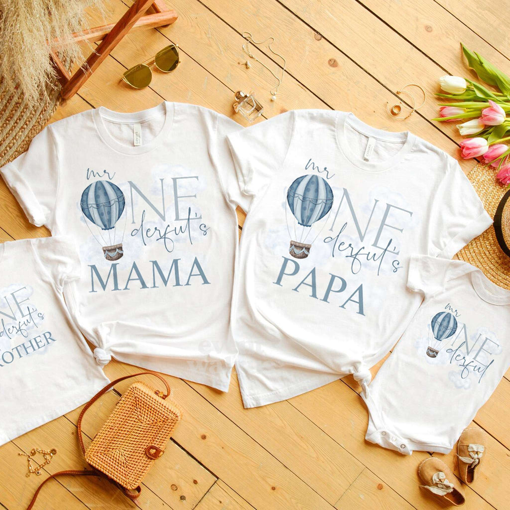 Mama, Papa and Brother Mr Onederful tees laid out on a wooden floor with tulips.