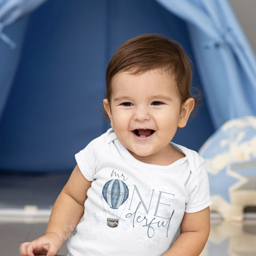 Smiling baby boy sitting in a white Mr Onederful bodysuit with a blue hot air balloon.