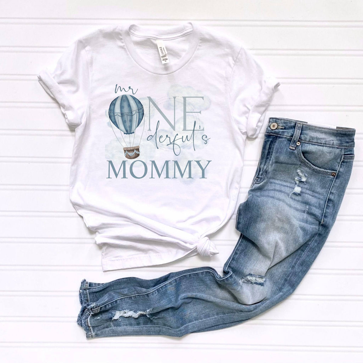 White Mr Onederful's Mommy adult tee laid flat beside ripped jeans.