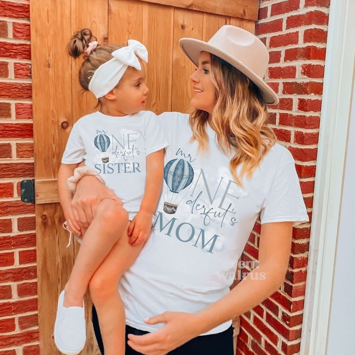 Toddler girl on her mom's hip, both in white hot air balloon Mr Onederful shirts.