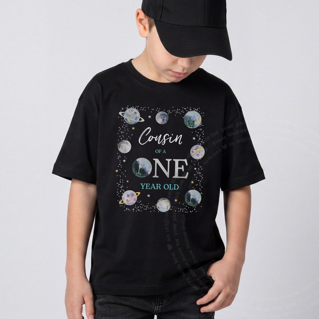 Boy in a black cap wearing a black Cousin of a ONE Year Old planet shirt.