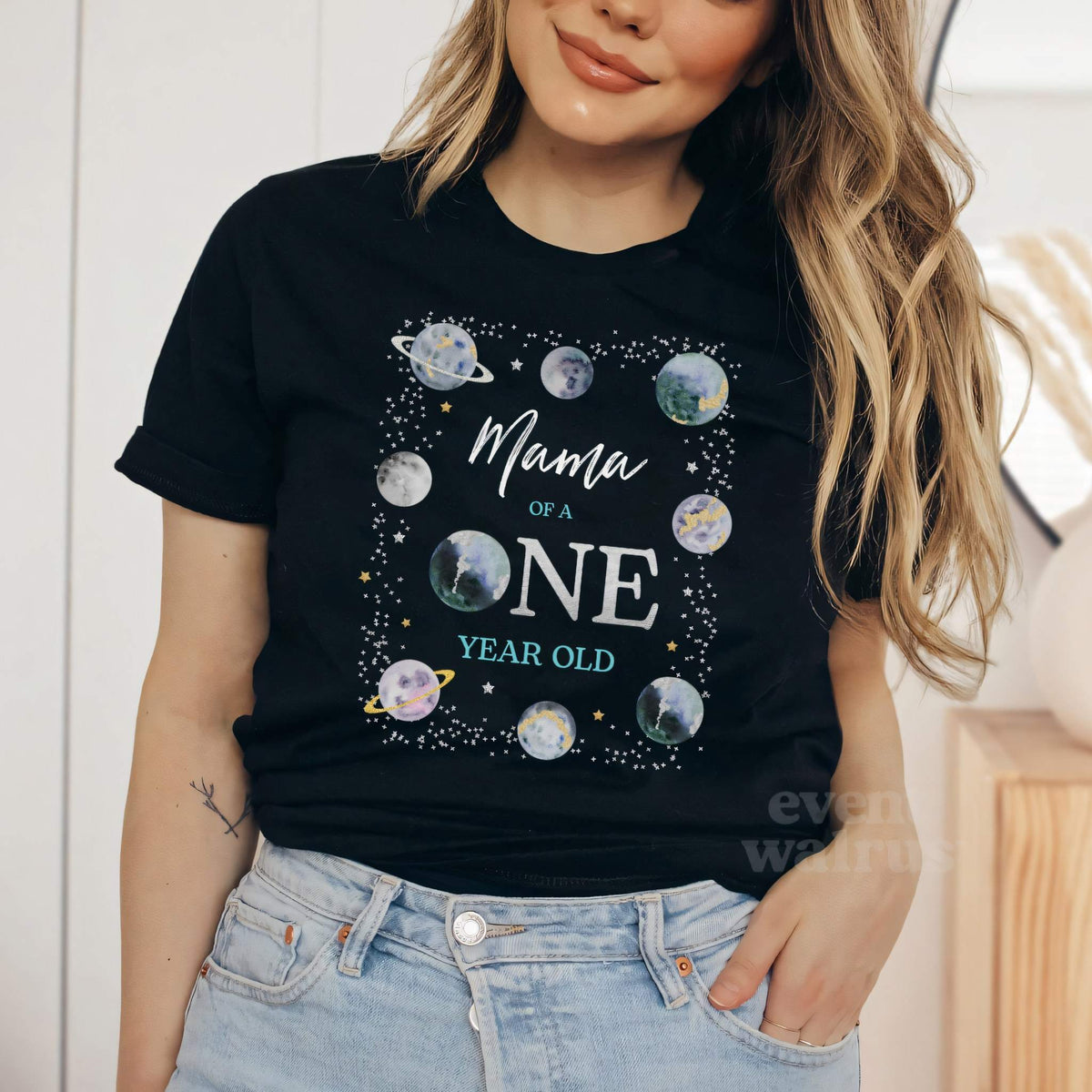 Woman in a black Mama of a ONE Year Old shirt framed by watercolor planets.