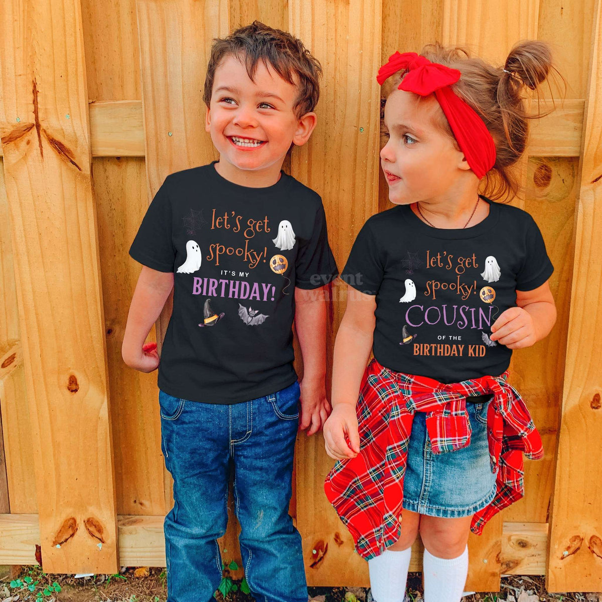 Boy and girl in black Let's Get Spooky Birthday and Cousin shirts by a wooden fence.