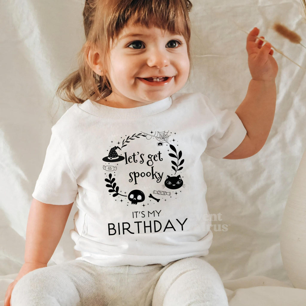 Laughing baby girl in a white Let's Get Spooky baby tee.