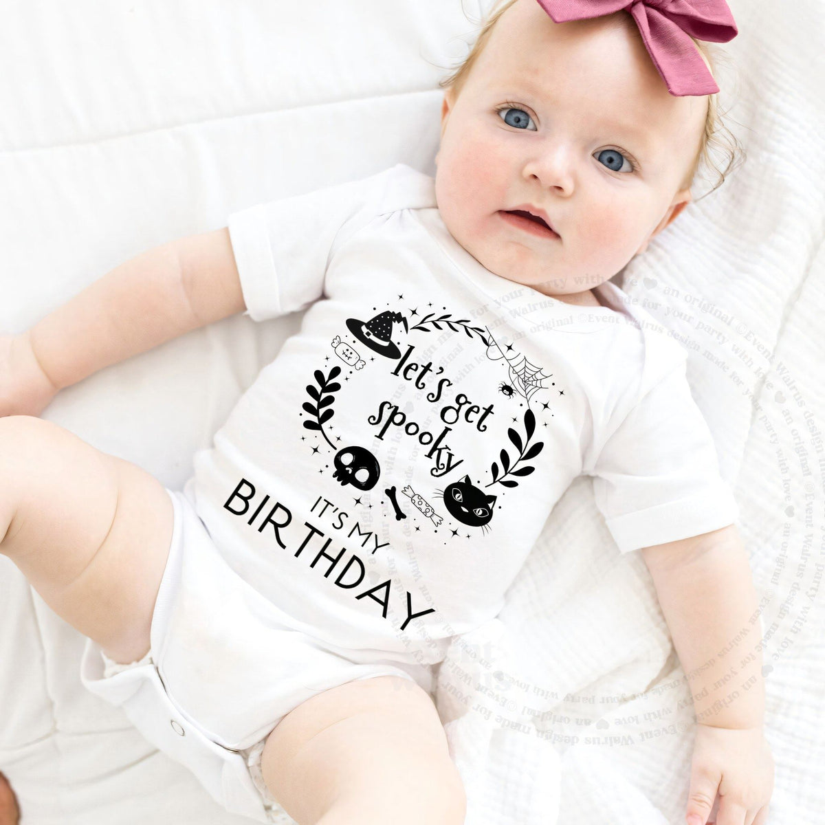 Baby girl with a pink bow lying in a white Let's Get Spooky It's My Birthday bodysuit.