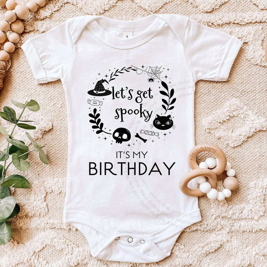 White Let's Get Spooky bodysuit on a beige blanket with a wooden teether.