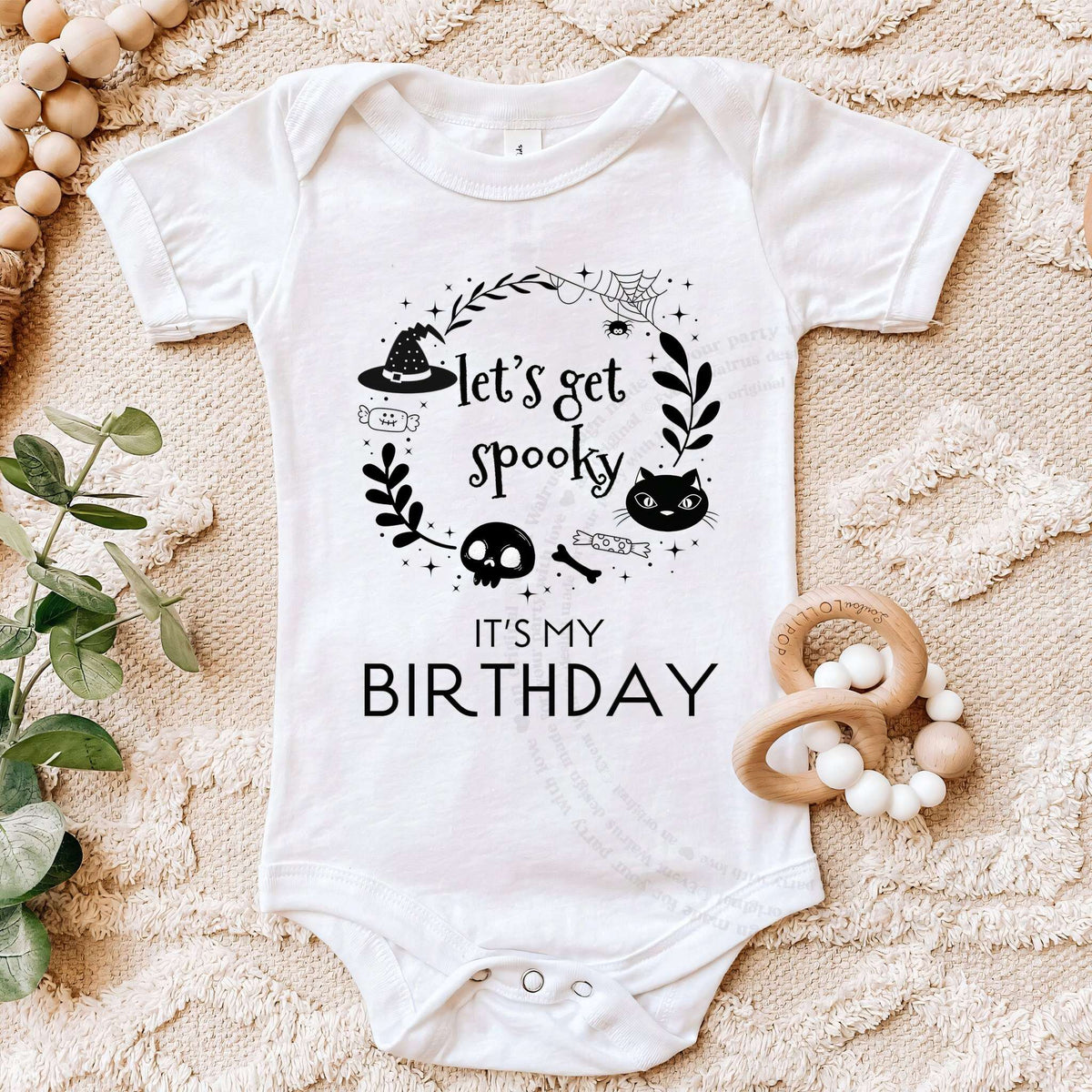 White Let's Get Spooky bodysuit on a beige blanket with a wooden teether.