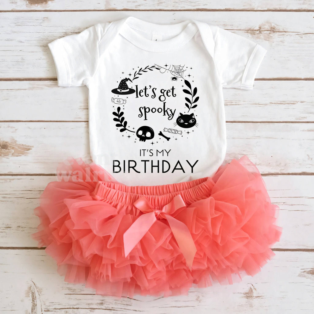 White Let's Get Spooky bodysuit laid flat with a coral tutu on whitewashed wood.
