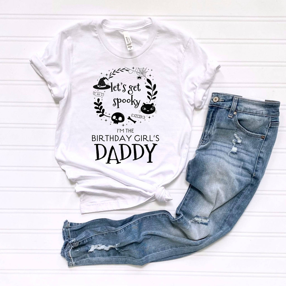 White Let's Get Spooky Daddy tee laid flat beside jeans.