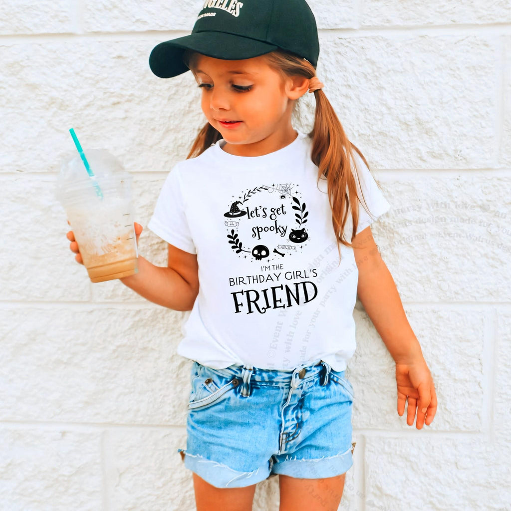 Girl in a ball cap holding a drink in a white Let's Get Spooky Friend shirt.