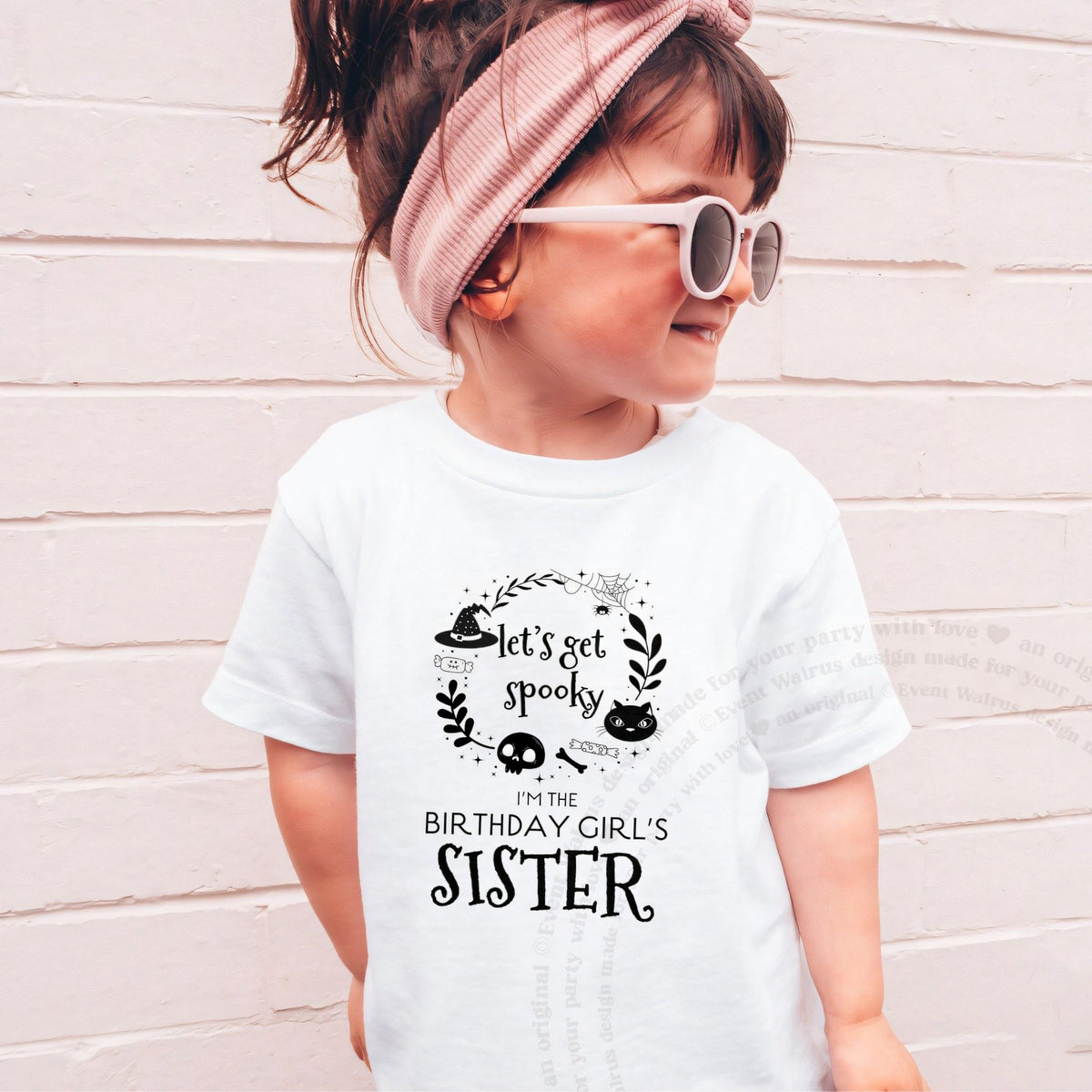 Girl in sunglasses and a pink headband wearing a white Let's Get Spooky Sister shirt.