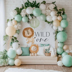 Lion Wild One banner indoors against white brick with a mint balloon arch, palm leaves and a lion pillow.