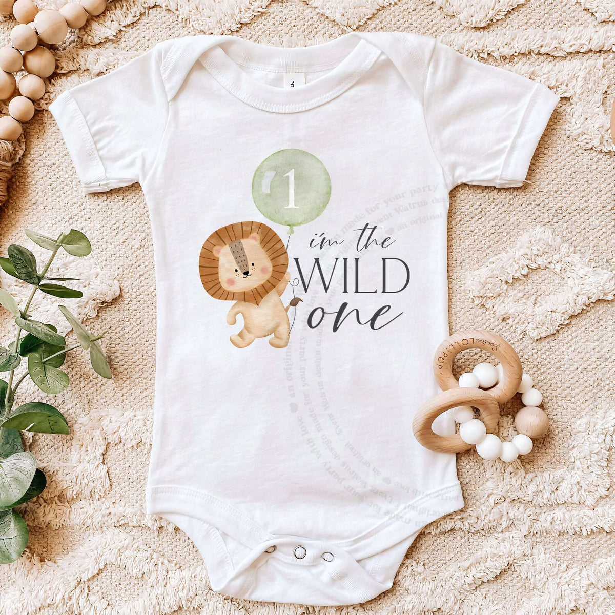 White I'm the Wild One bodysuit on a beige blanket with a wooden teether.