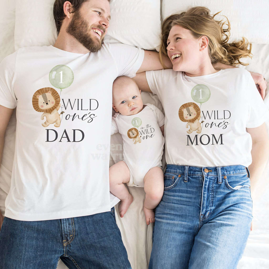 Dad and Mom lying beside their baby, all three in white lion Wild One shirts.