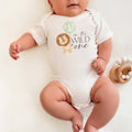 Baby lying on a white blanket in an I'm the Wild One bodysuit with the lion and sage balloon.