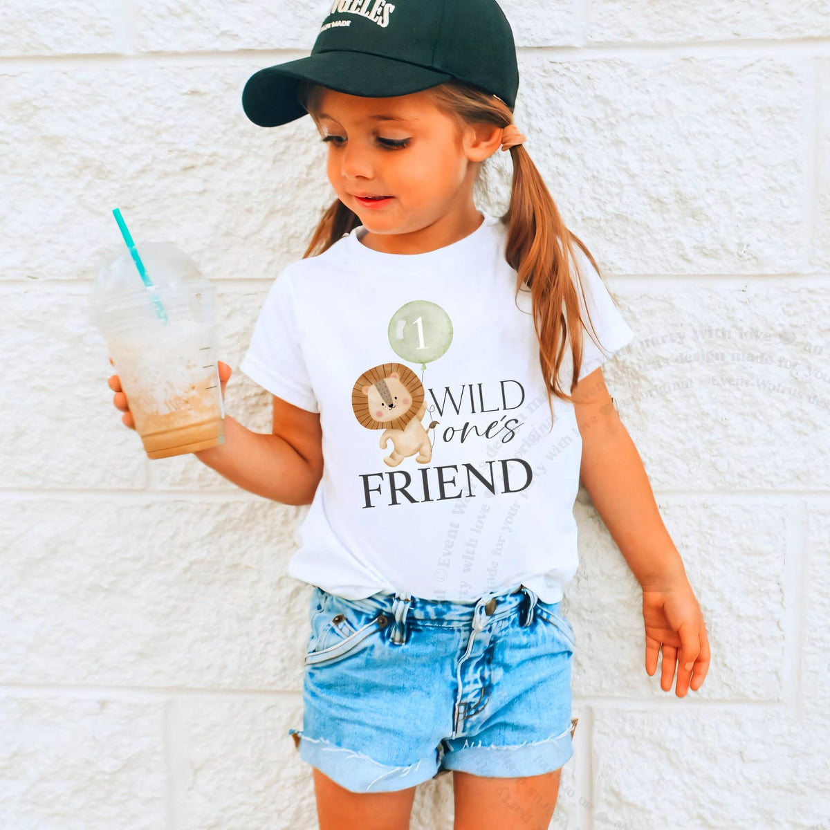 Girl in a ball cap holding a drink in a white Wild One's Friend shirt.