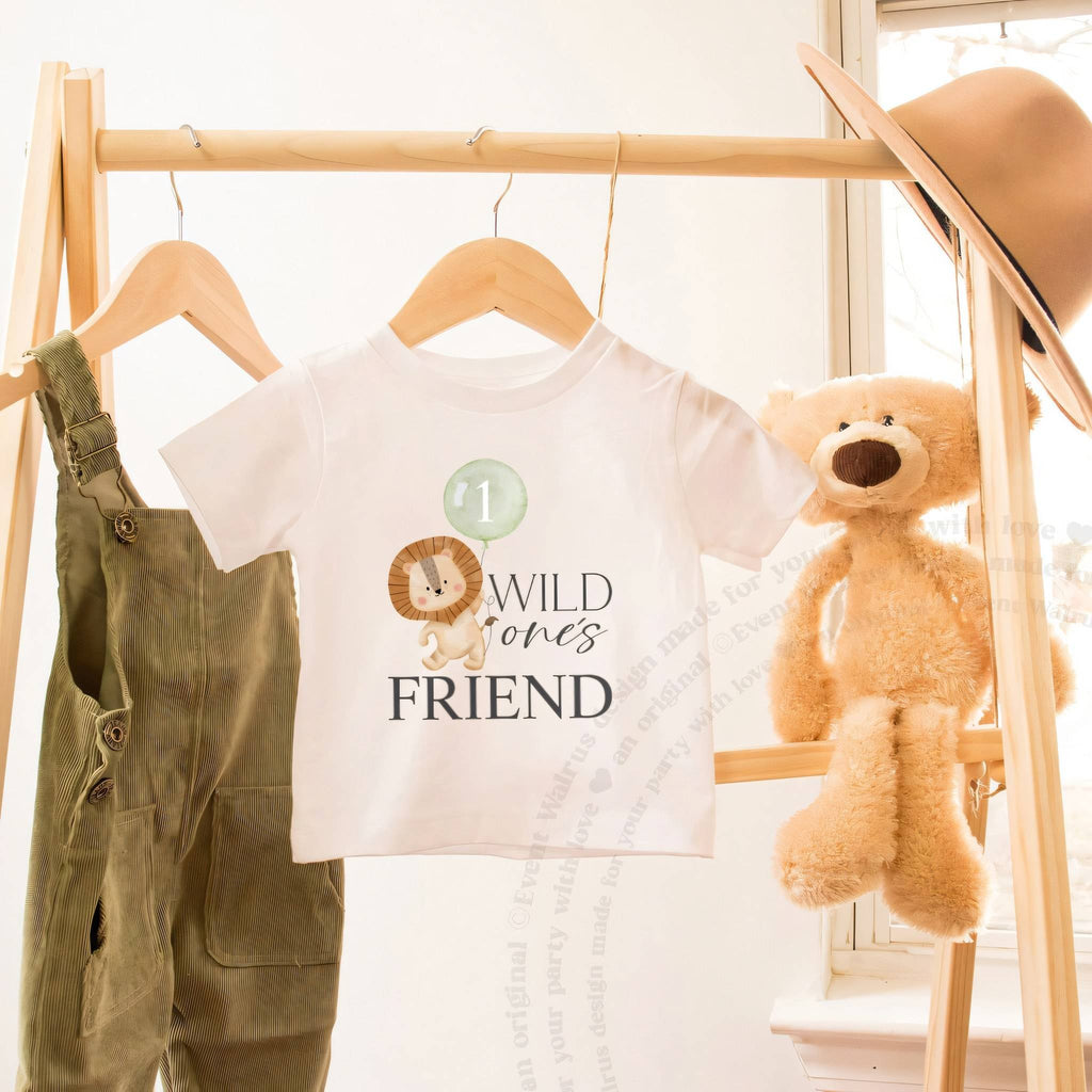 White Wild One's Friend toddler tee on a wooden clothes rack beside a teddy bear.