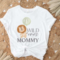 White Wild One's Mommy adult tee laid flat on a round jute rug with dried palm leaves.