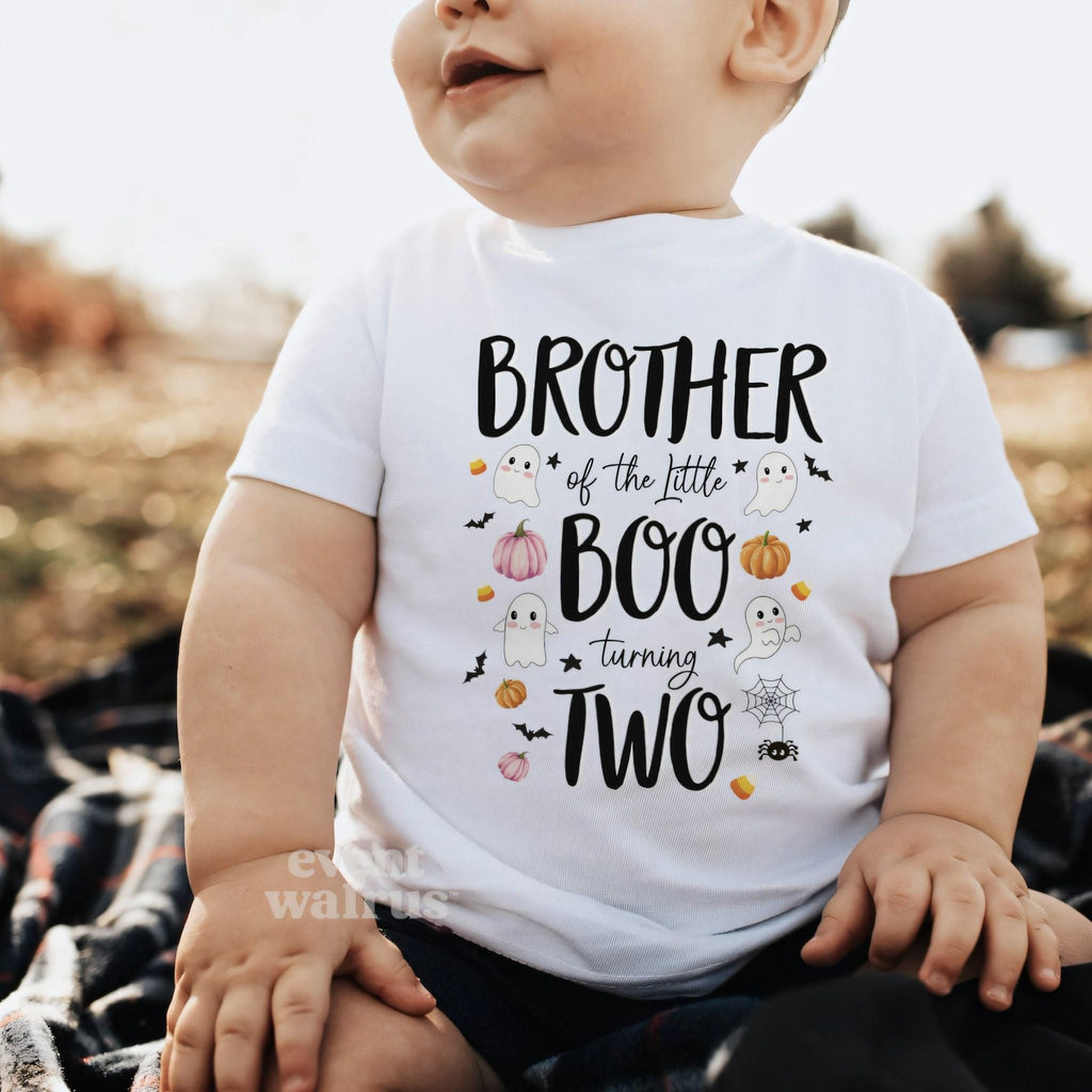 Baby sitting outdoors on a blanket in a white Brother of the Little Boo baby tee.
