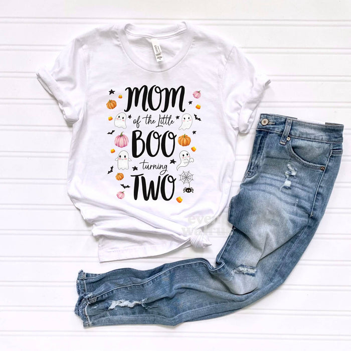 White Mom of the Little Boo Turning Two tee laid flat beside ripped jeans.