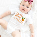 Baby girl with a pink bow in a white I'm the Little Cutie bodysuit with a clementine.