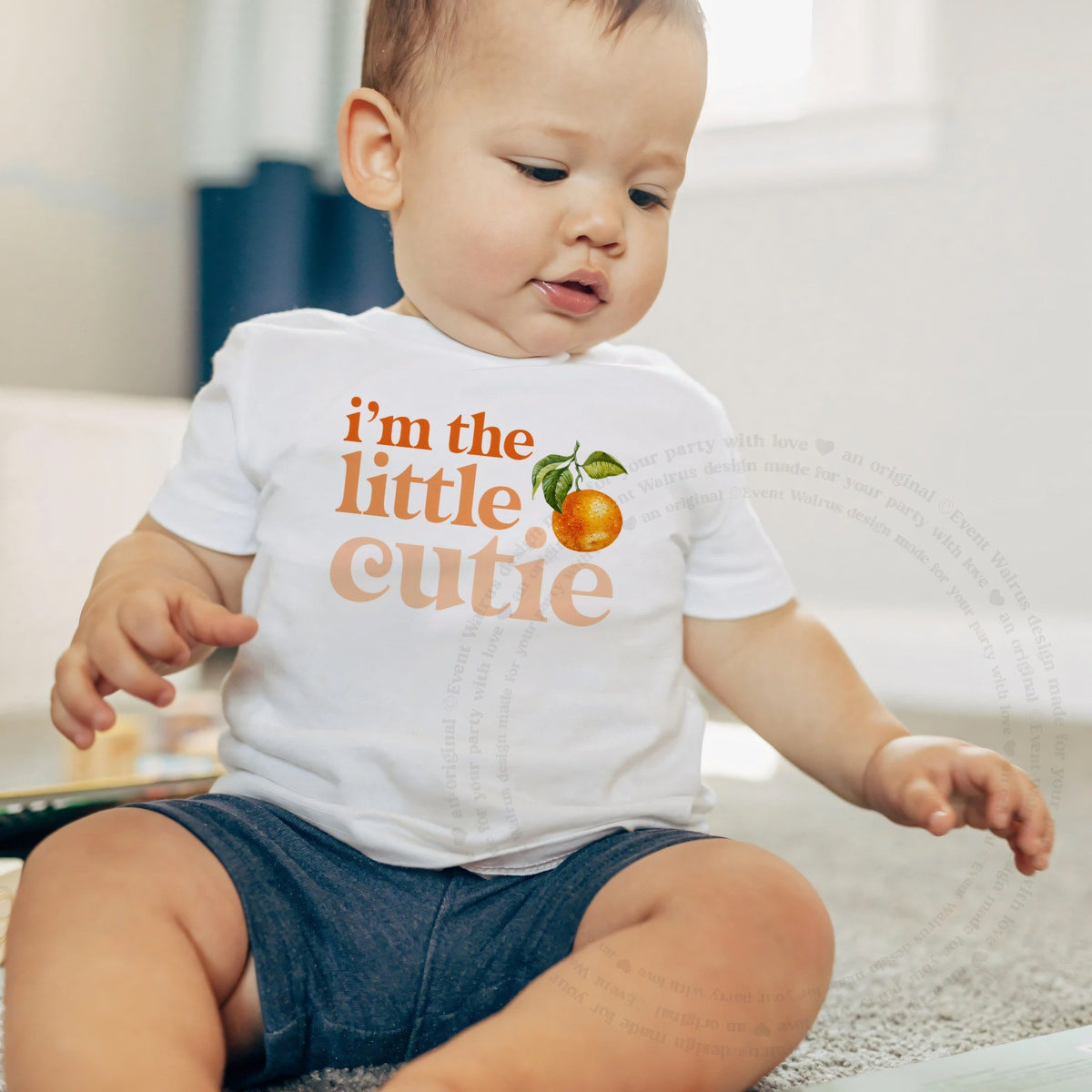Baby boy sitting on a rug in a white I'm the Little Cutie baby tee.