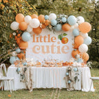 Little cutie backdrop behind a white dessert table with peach, white and blue balloons.