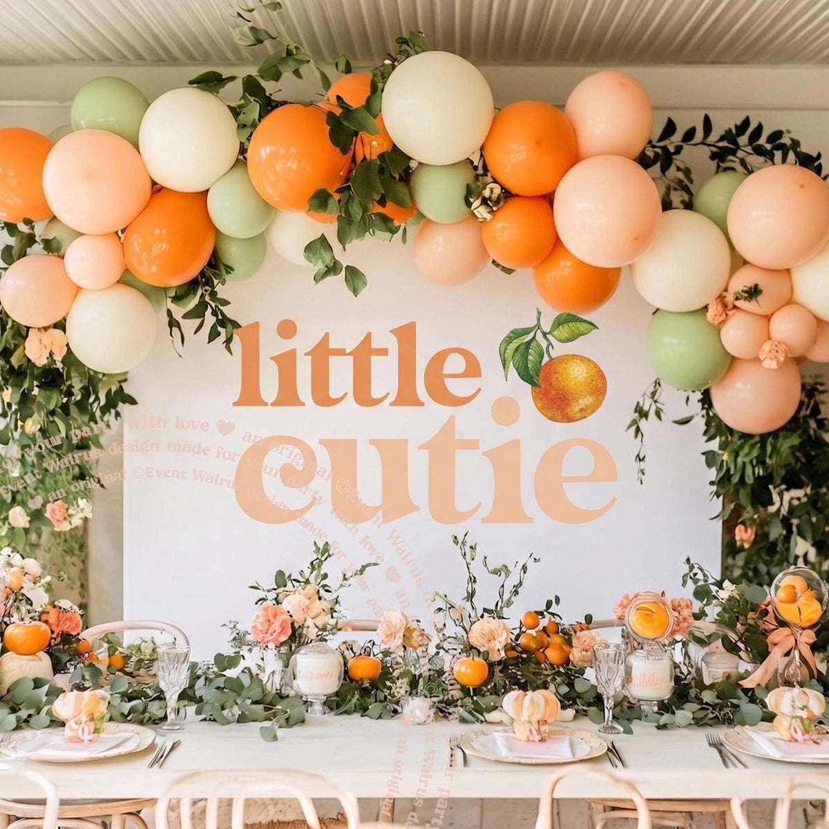 Little cutie backdrop above a long table with orange balloons and fresh flowers.