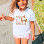 Laughing girl on a sidewalk in a white Cousin of the Little Cutie shirt.