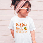 Girl in a pink headband and sunglasses wearing a white Sister of the Little Cutie tee.
