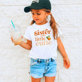 Girl in a black cap holding a drink in a white Sister of the Little Cutie tee.