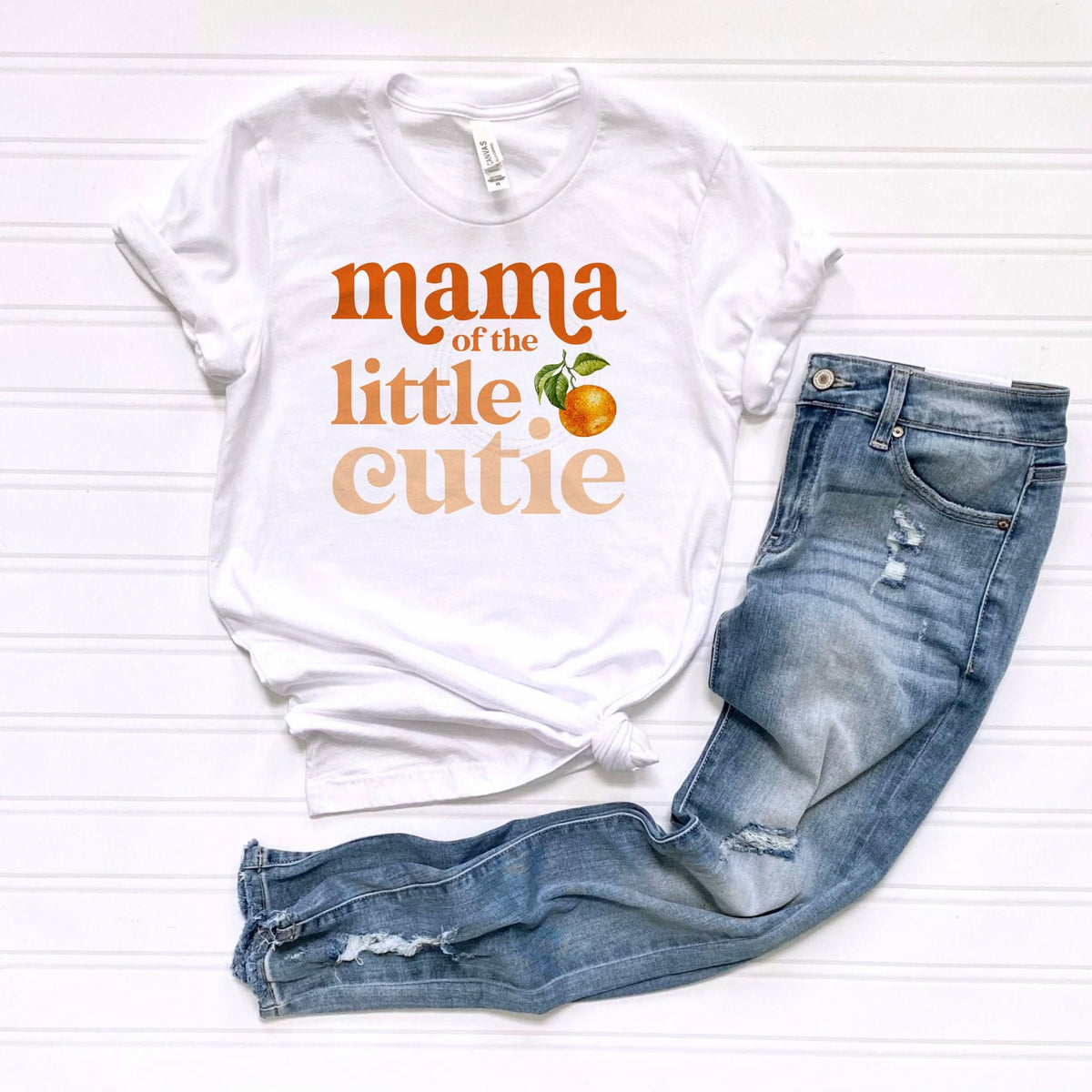 White Mama of the Little Cutie tee laid flat beside light blue jeans.