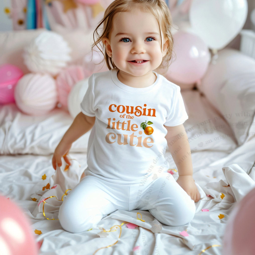 Smiling toddler among pink balloons in a white Cousin of the Little Cutie tee.