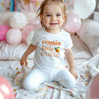 Smiling toddler among pink balloons in a white Cousin of the Little Cutie tee.