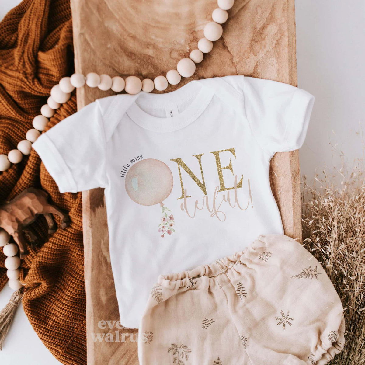 White Little Miss Onederful baby bodysuit laid flat with bloomers and a wooden bead garland.
