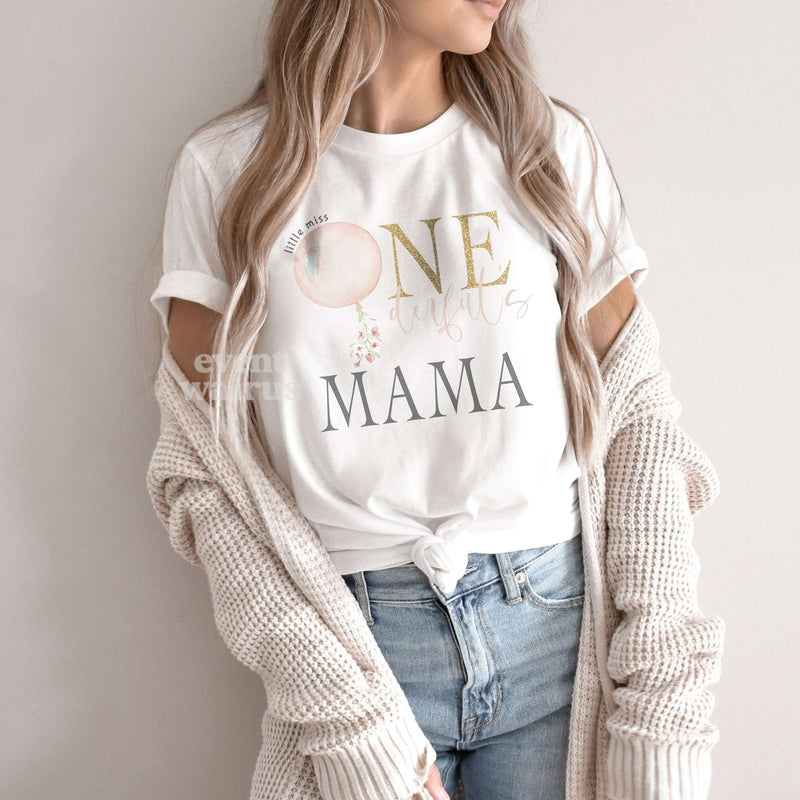 Woman in a cardigan wearing a white Mama shirt with a pink balloon and gold ONE.
