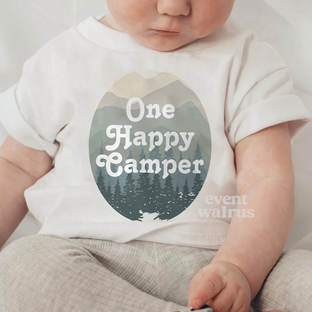 Baby sitting up in a white One Happy Camper baby tee.
