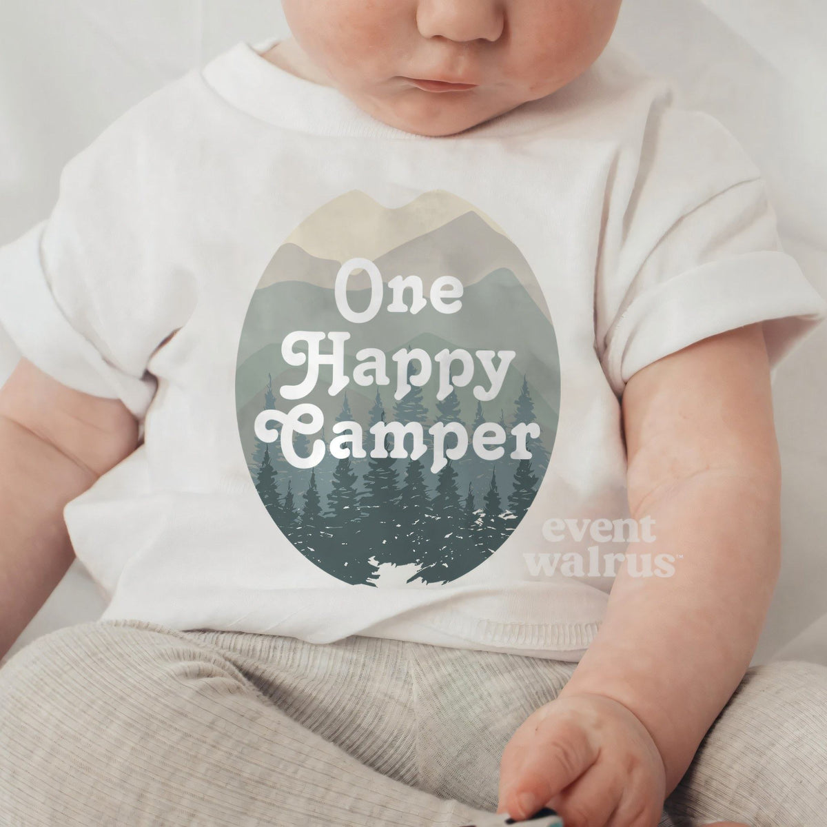 Baby sitting up in a white One Happy Camper baby tee.