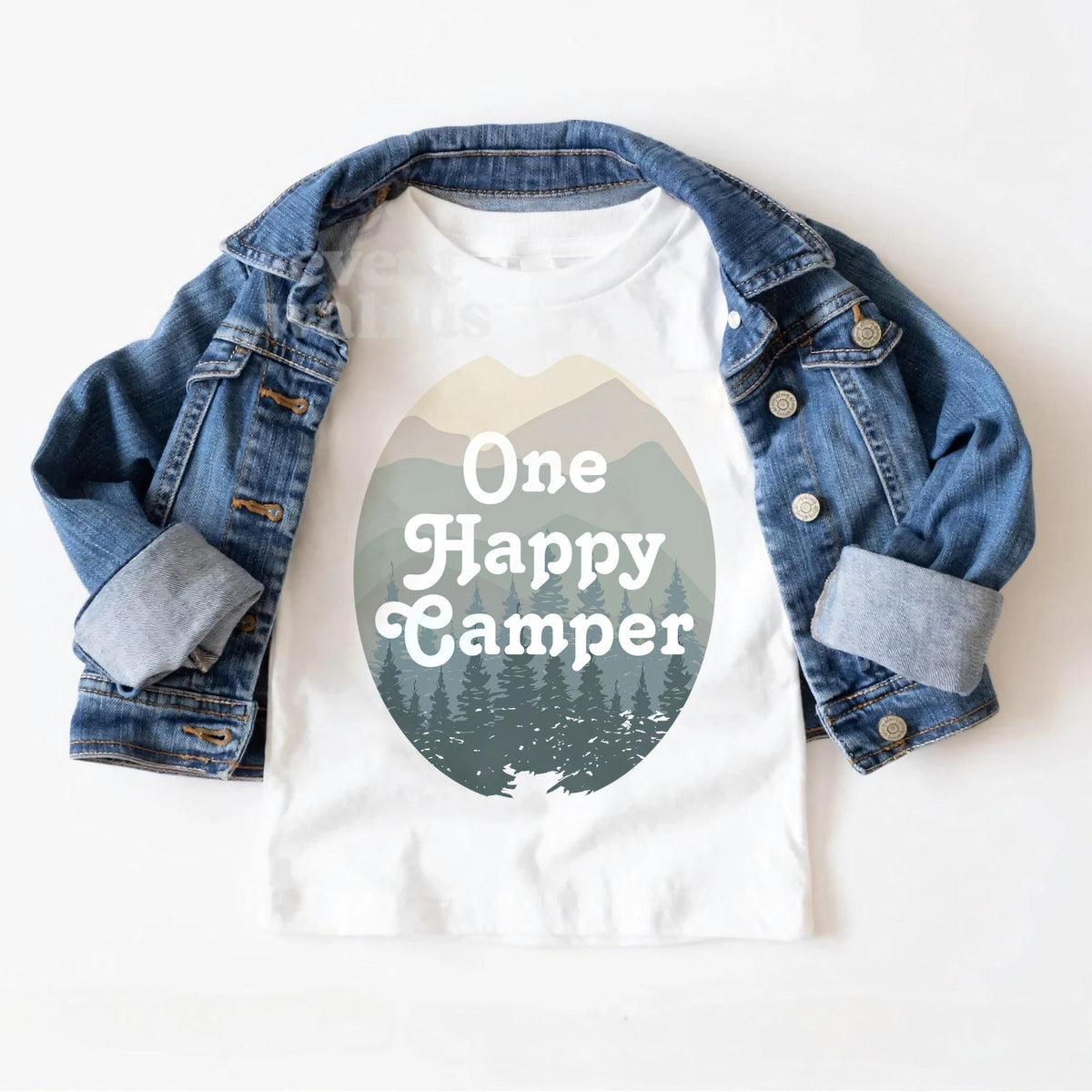 White One Happy Camper toddler tee laid on a denim jacket.