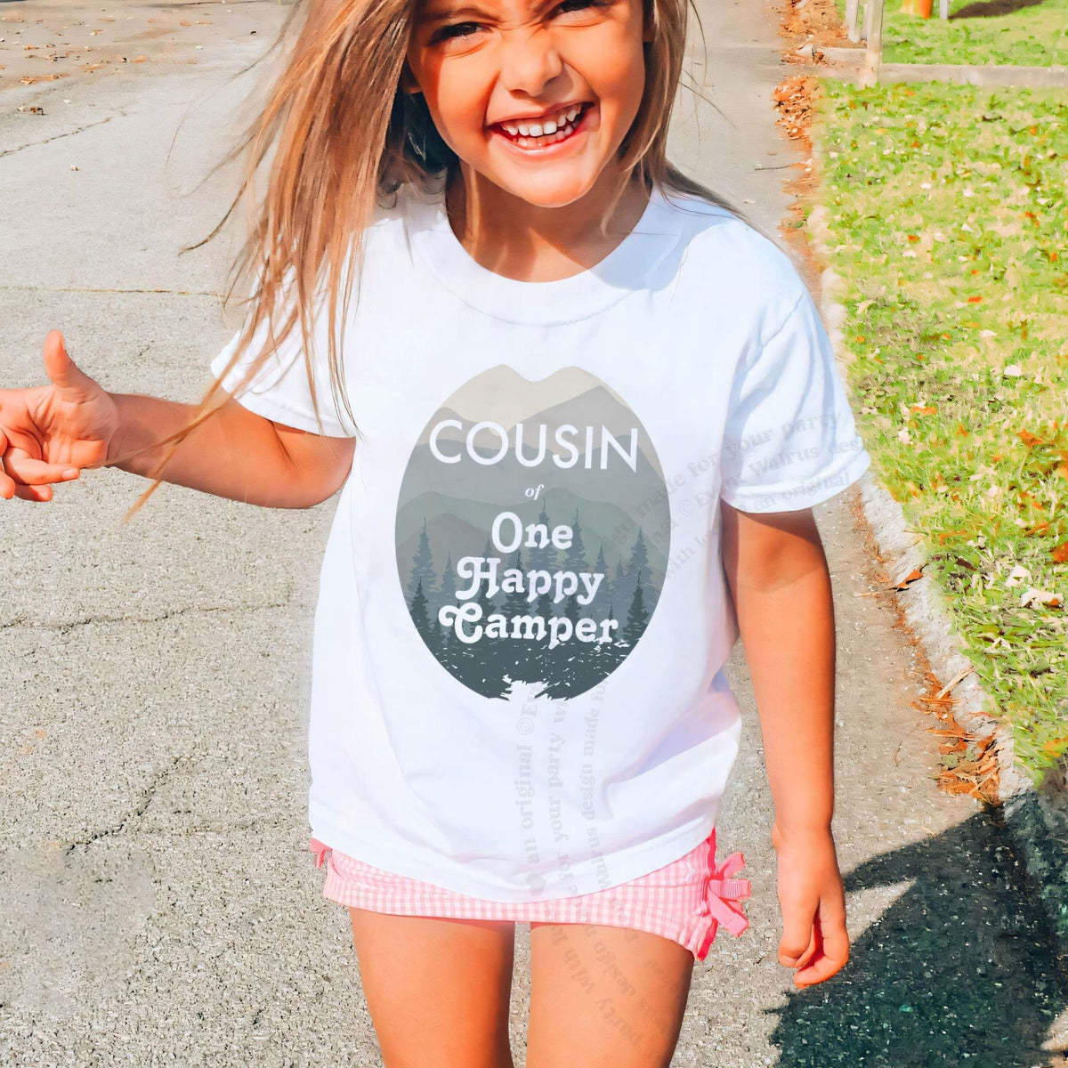 Laughing girl outdoors in a white Cousin of One Happy Camper kids tee.