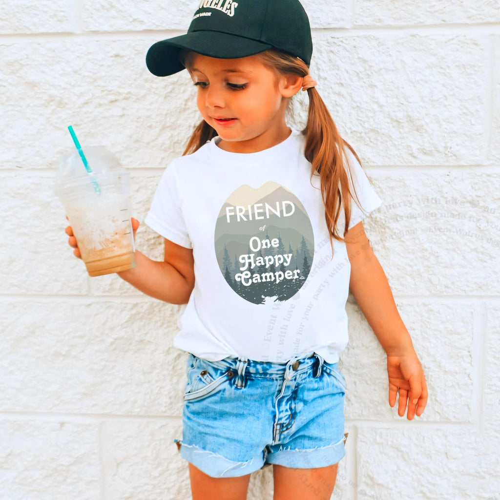 Girl in a ball cap holding a drink in a white Friend of One Happy Camper shirt.