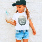 Girl in a ball cap holding a drink in a white Friend of One Happy Camper shirt.