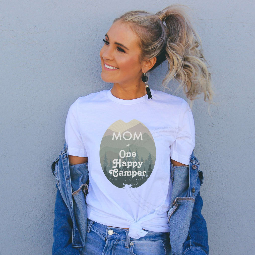 Smiling woman in a denim jacket wearing a white Mom of One Happy Camper shirt.